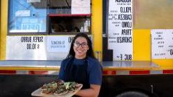 young hispanic woman standing in front of food truck with a tray of tacos